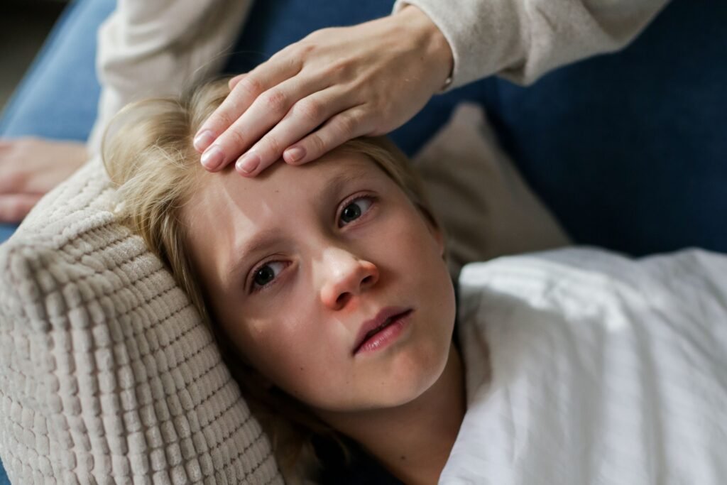 Sick girl lying in bed while a parent checks her forehead for fever