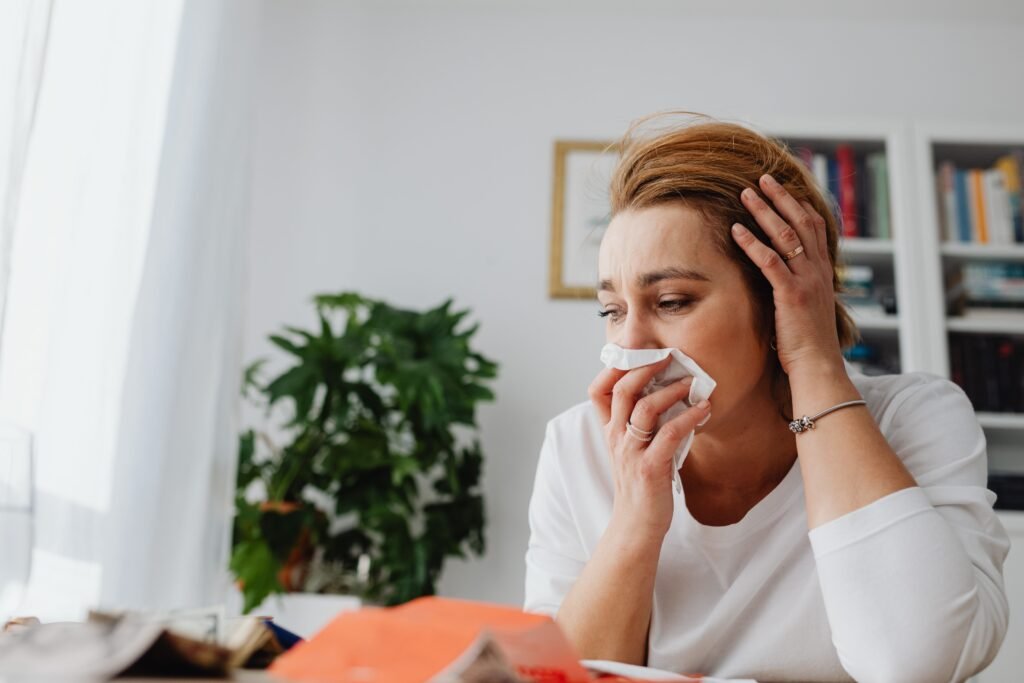 Woman sneezing into a tissue while sitting at a desk