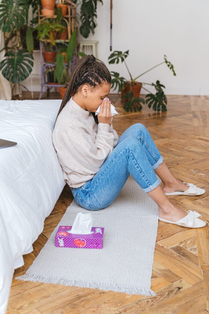 Young woman sitting on the floor blowing her nose with a box of tissues beside her