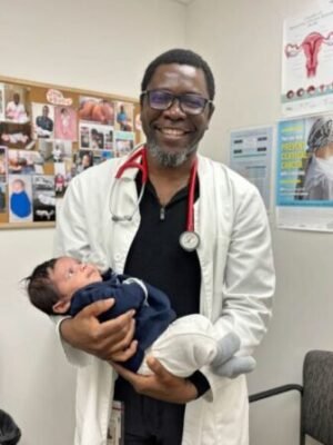 Doctor in a white coat smiling while holding a newborn baby